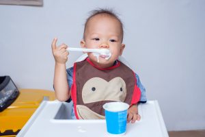 Smile Asian Toddler boy using spoon eating yogurt